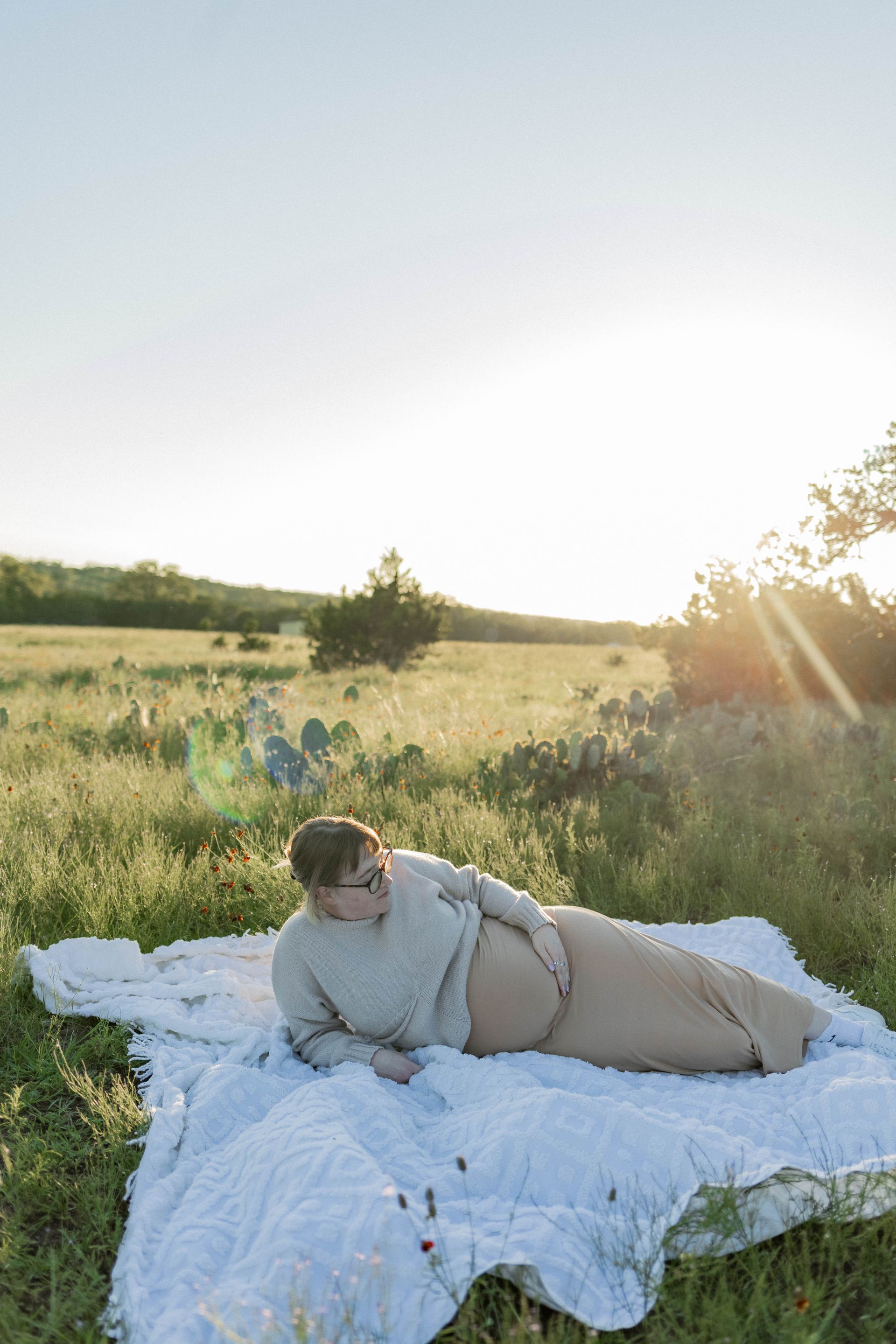 Person lying on a white blanket in a sunlit grassy field at sunset.