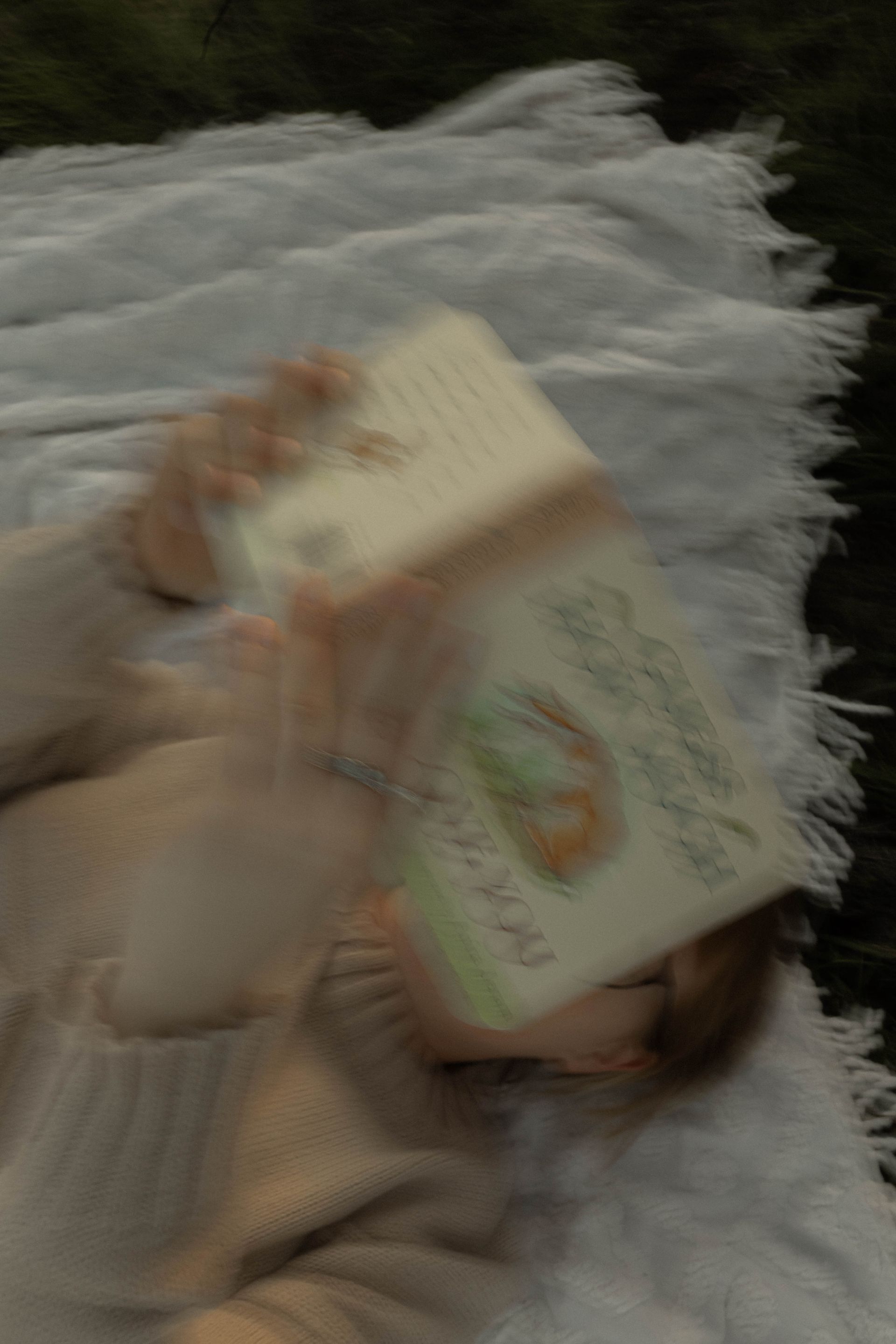 Person lying on a bed holding two illustrated books, one cream and one green.