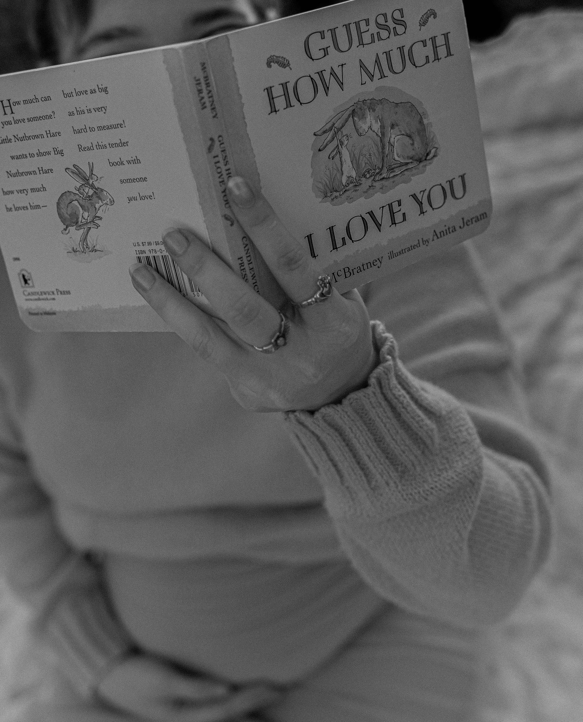 Person reading a book titled “Guess How Much I Love You” while lying on a couch.