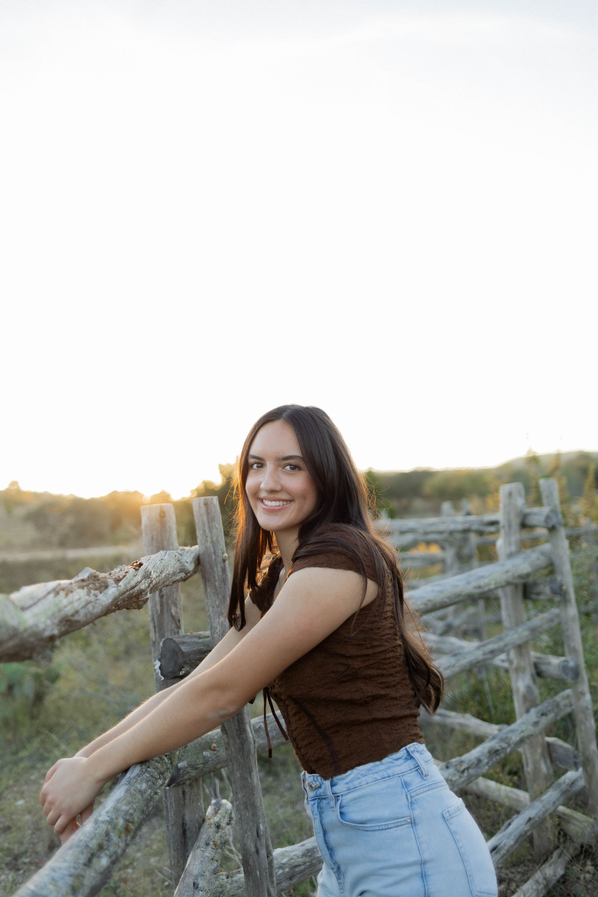 Woman smiling and leaning on a wooden fence at sunset in a rustic field