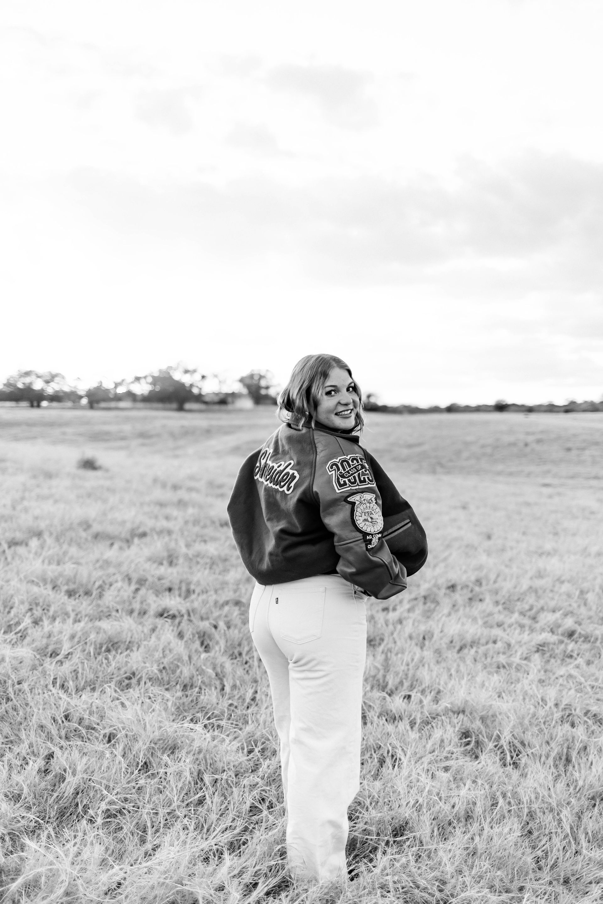 Person standing in a grassy field, looking back over their shoulder in a black-and-white photo.