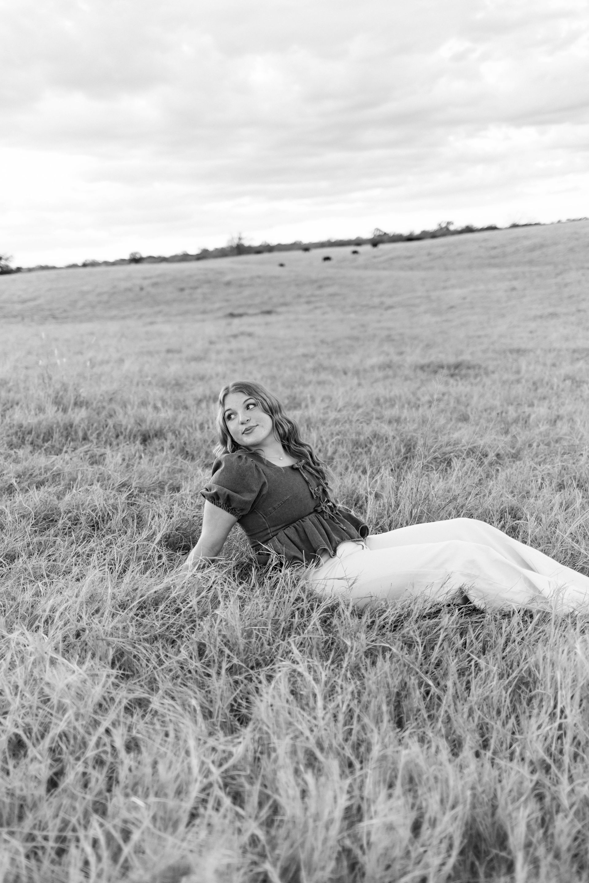 Person reclining in tall grass in a black-and-white field, looking toward the camera.