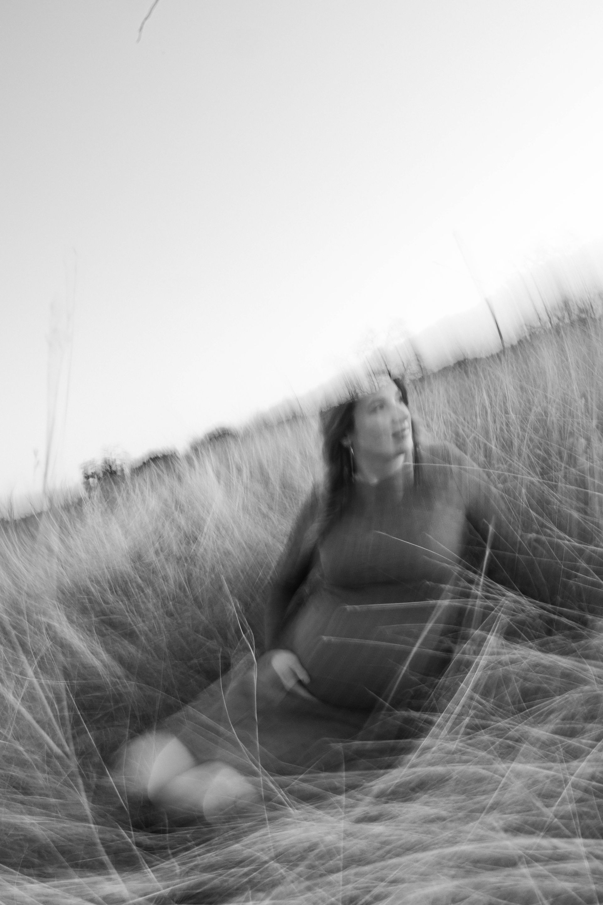 Blurry black-and-white person sitting in tall grass on a hillside