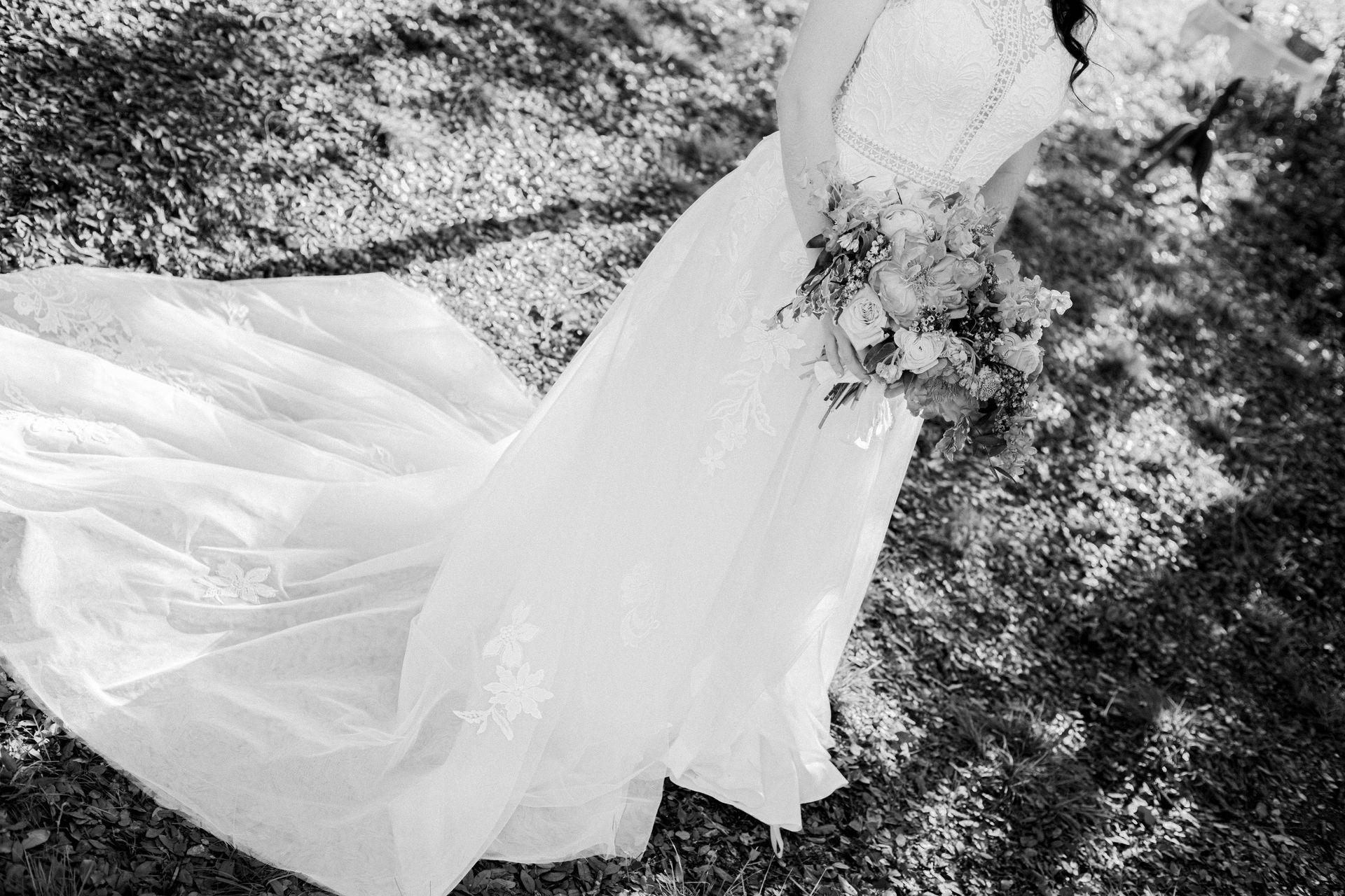 White bridal gown with a long train laid on grass in black and white.