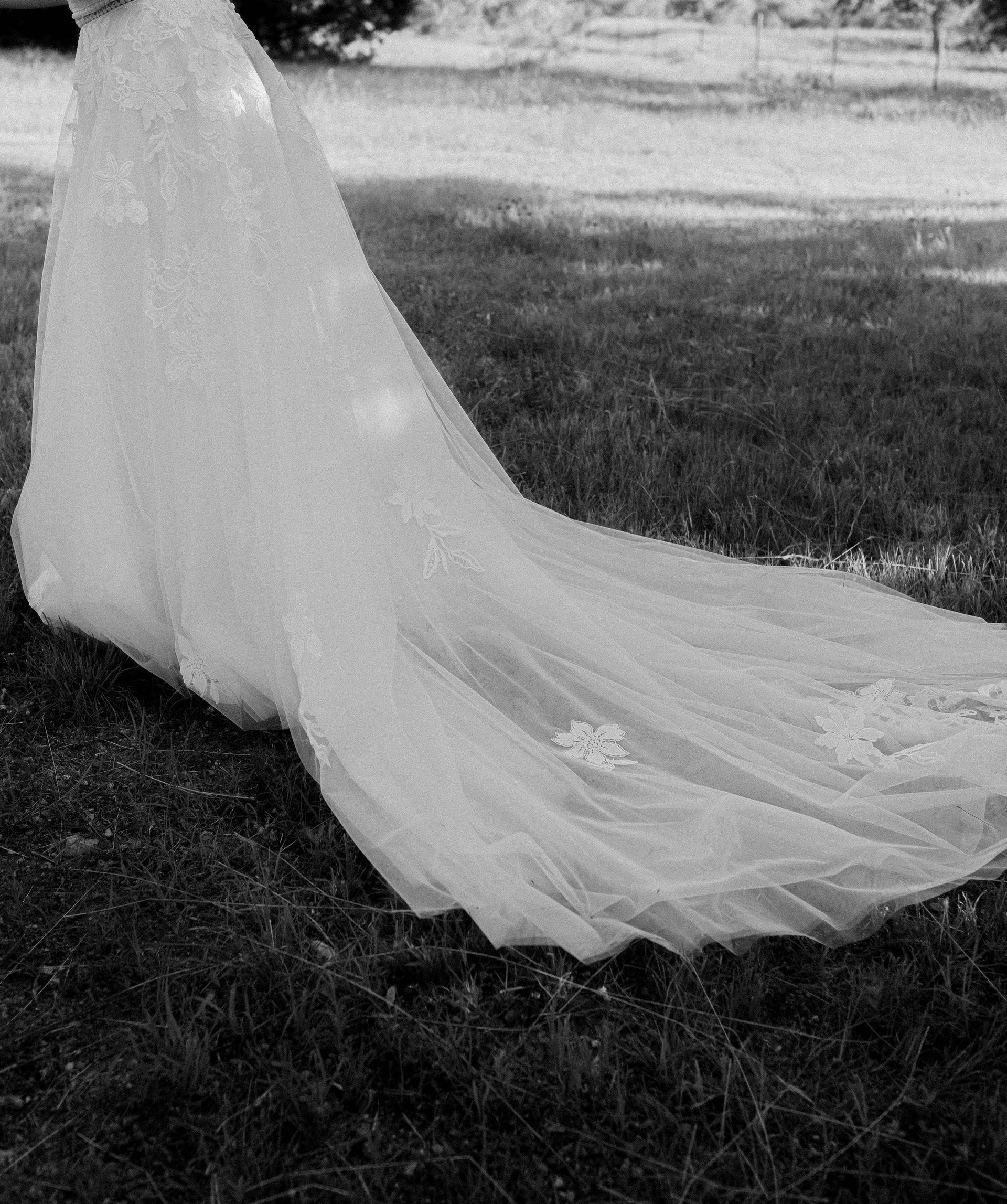 Long white bridal veil draped over grass, trailing across the ground outdoors