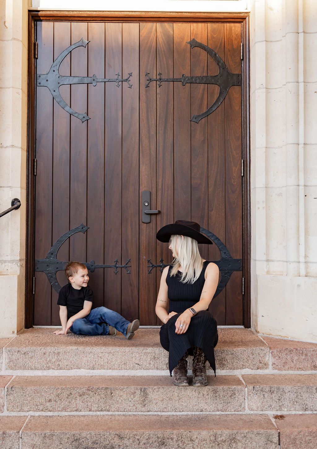 Two people sitting on stone steps before a large wooden door with metal hinges