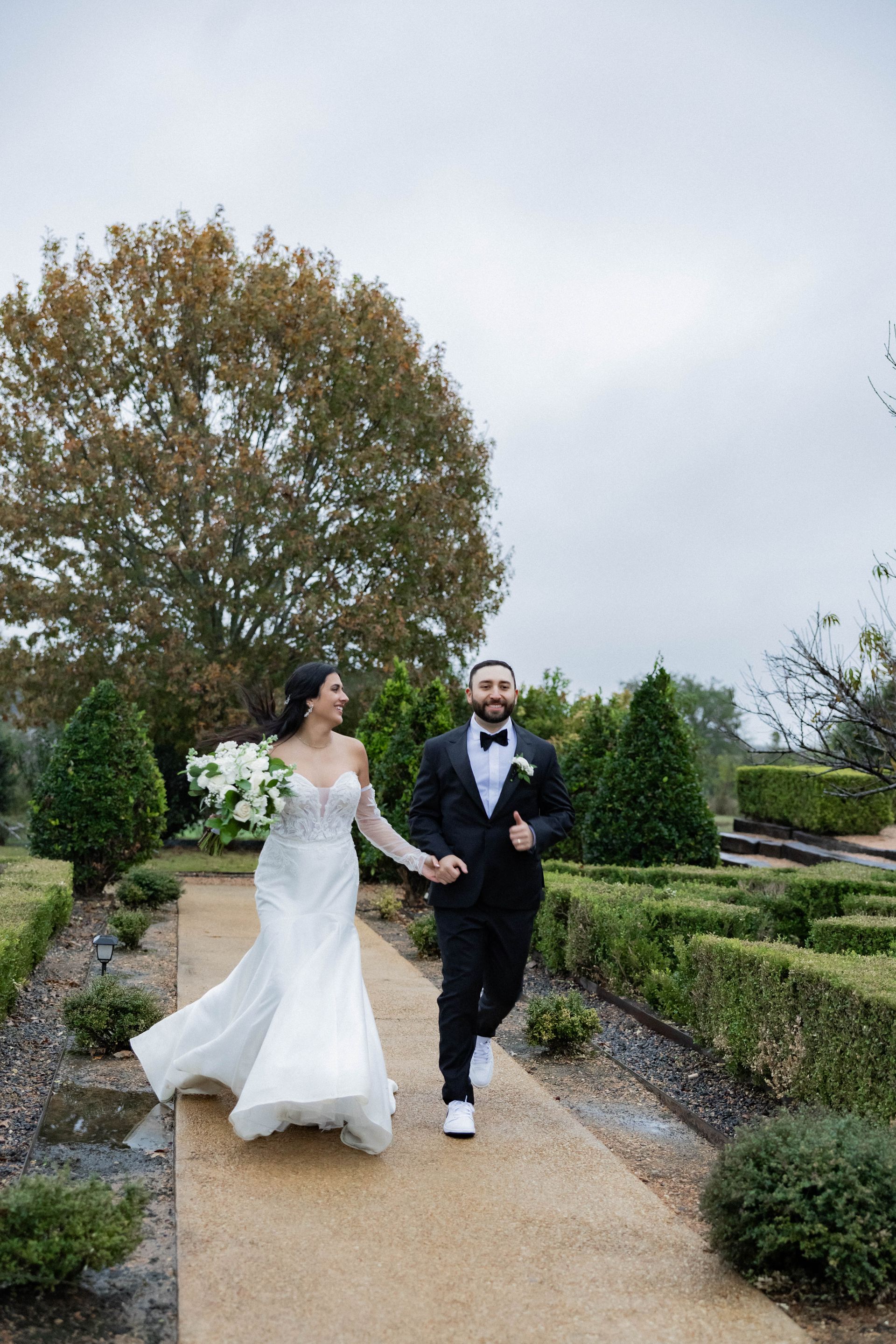Bride and groom running hand in hand along a garden path outdoors