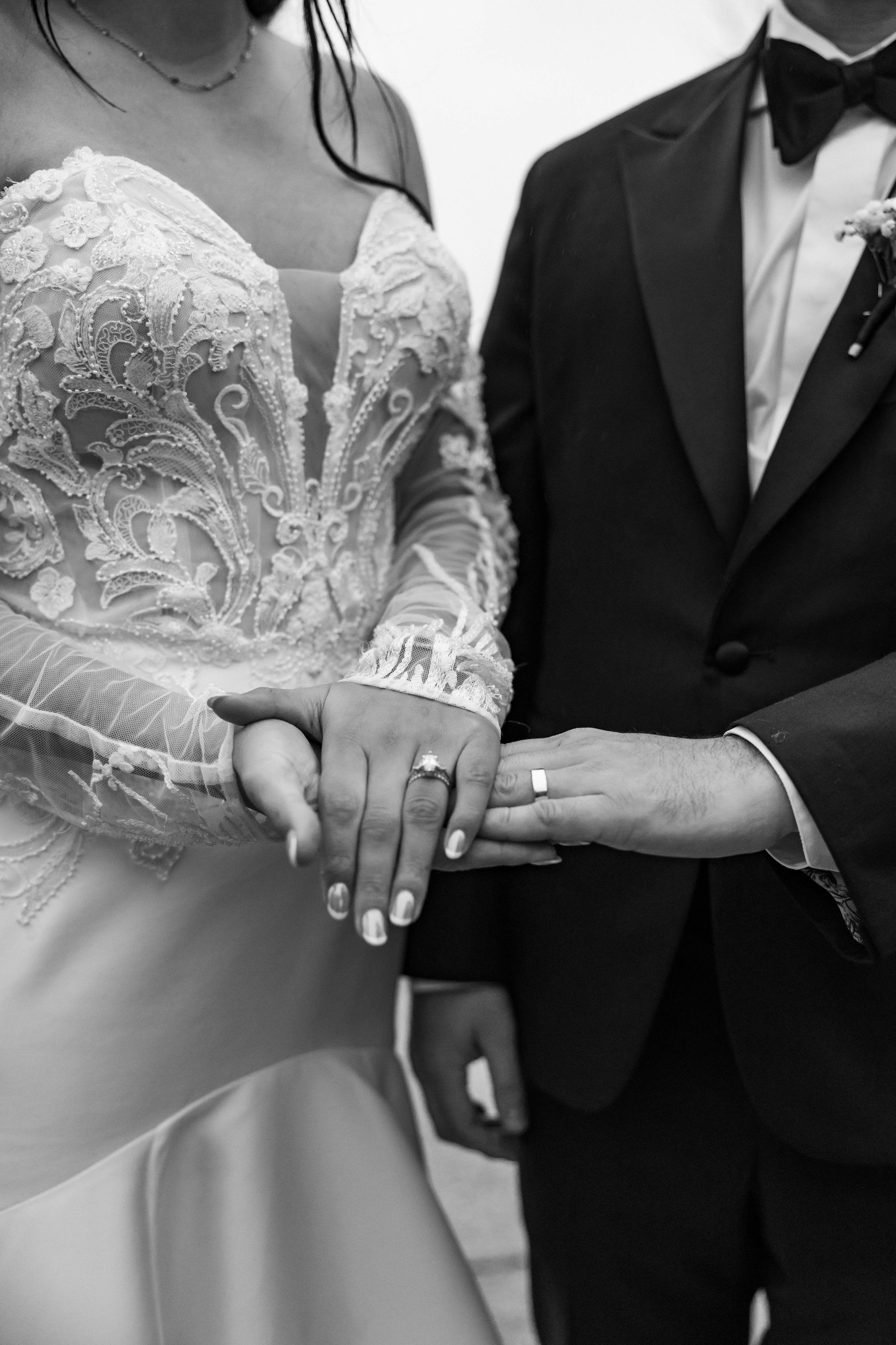 Bride and groom holding hands in wedding attire, close-up in black and white.