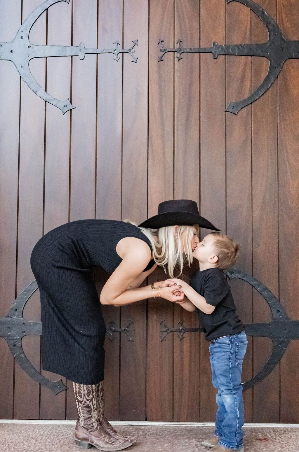 Woman and child kissing in front of a wooden barn door with metal hinges
