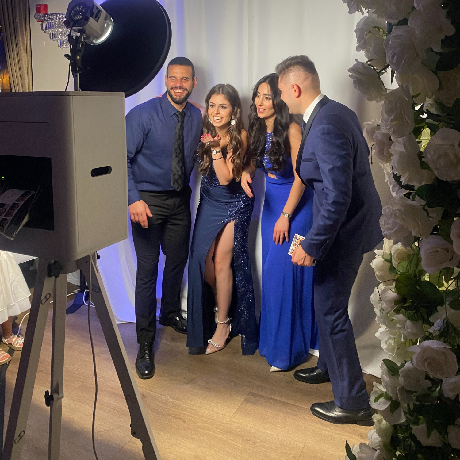 Four people posing in formal blue outfits at an indoor event photo booth