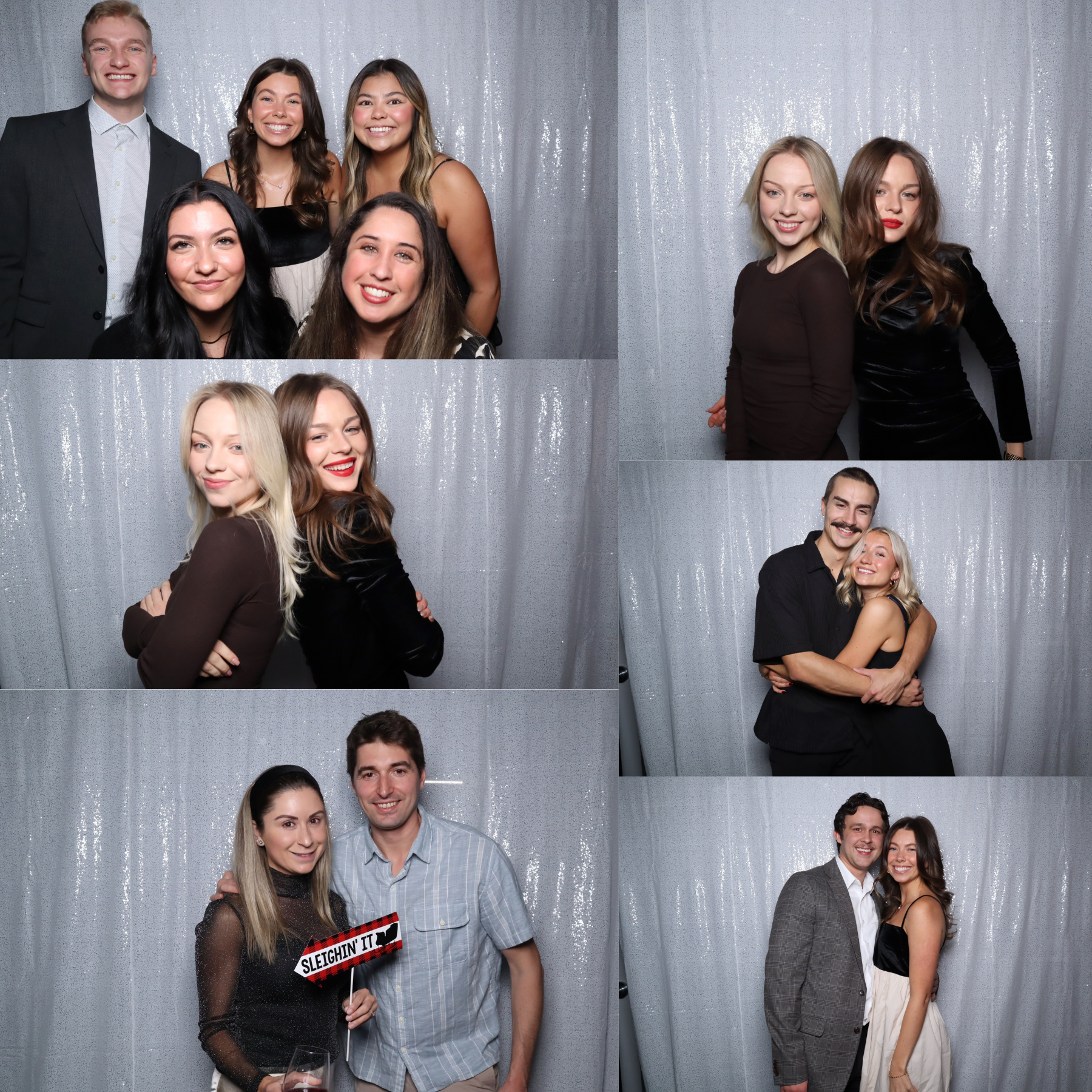 Group of adults posing in a photo booth against a silver backdrop, smiling and hugging in formal attire