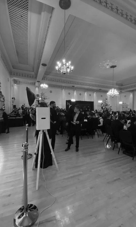 Black-and-white view of a formal banquet hall with guests seated at round tables and a speaker stand in the foreground