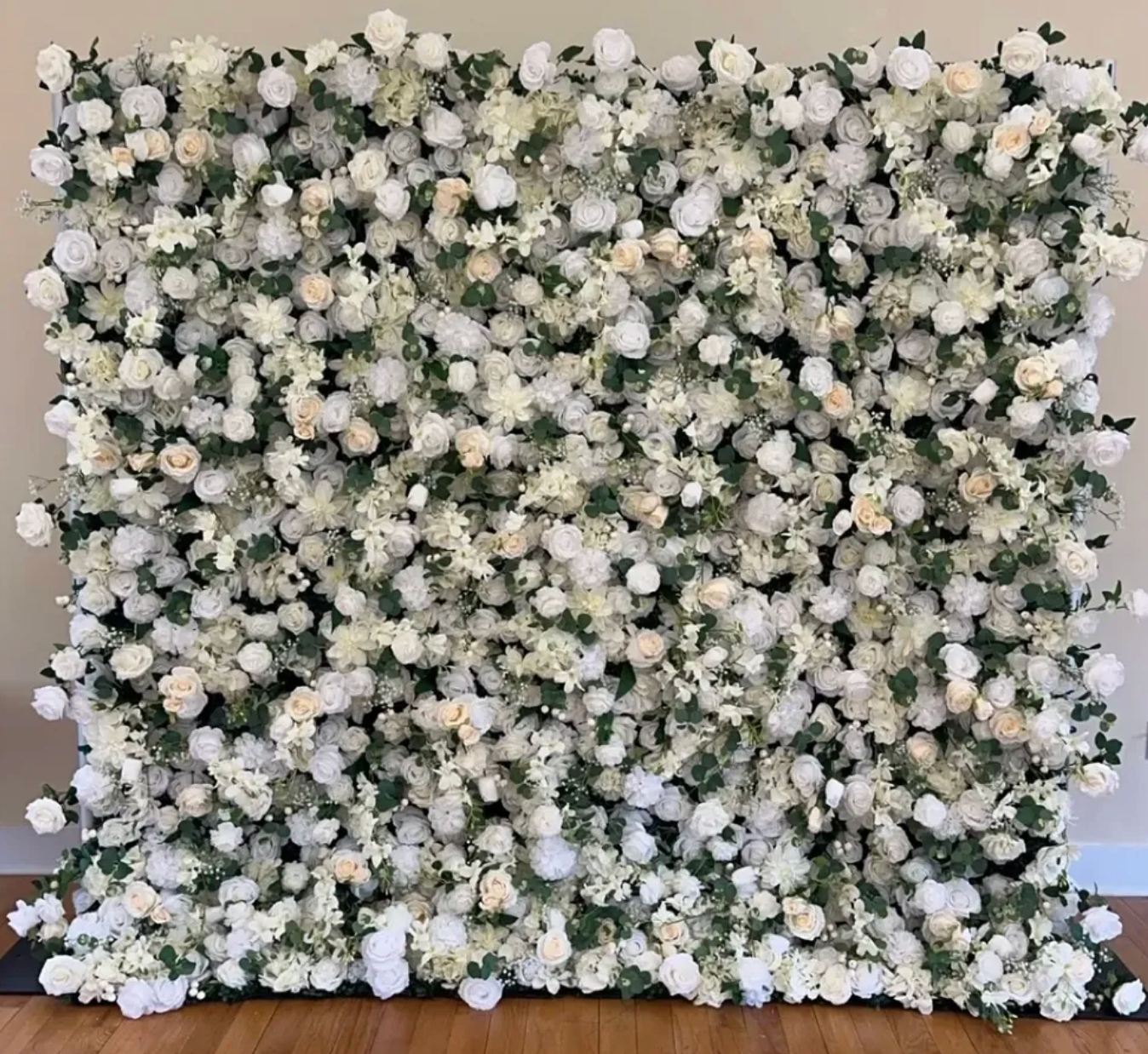 White and cream flower wall backdrop with dense greenery on a wooden floor
