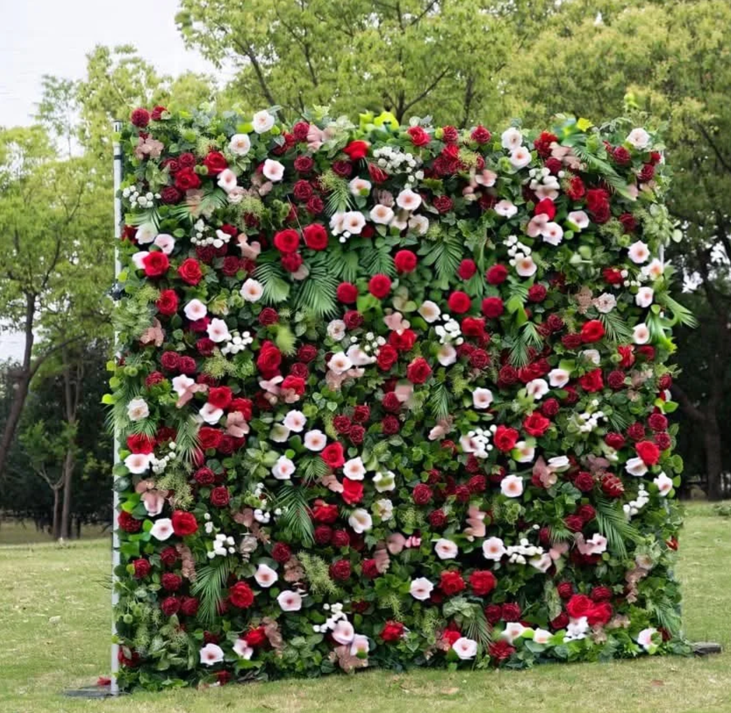 Square floral wall covered with red, white, and pink flowers in a grassy park