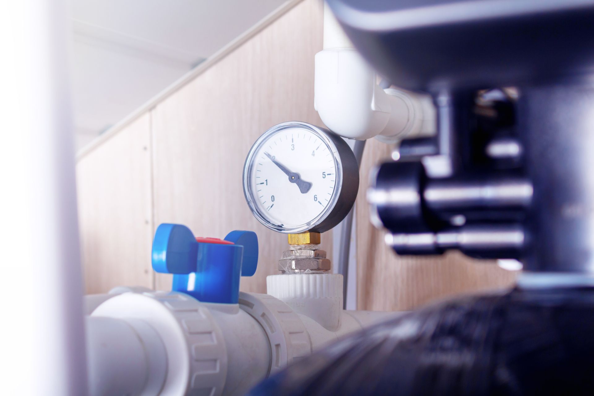 Pressure gauge and blue valve on a white pipe in an industrial setting, with machinery in the foreground