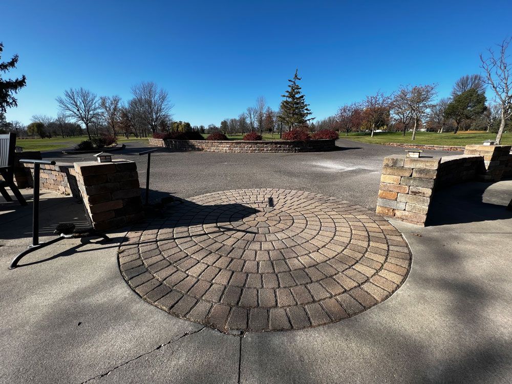 Brick patio with curved pattern, stone structures, and a clear blue sky.