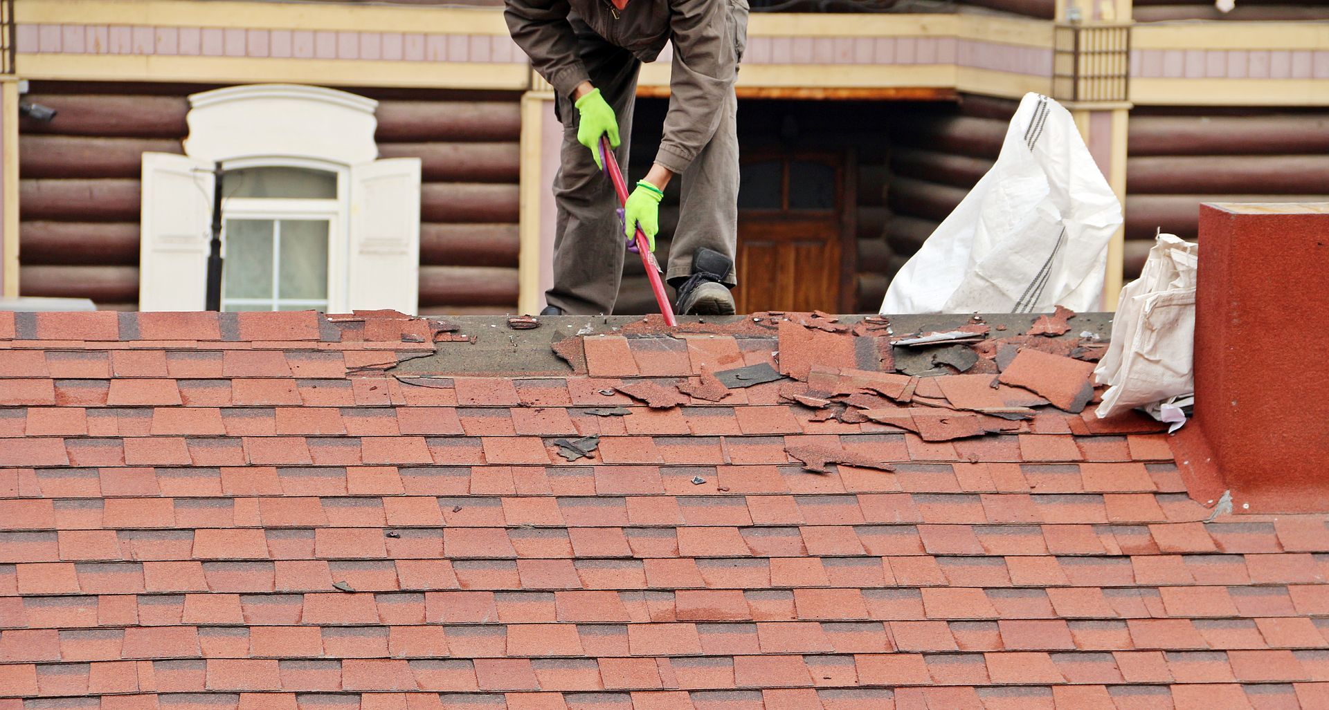 A man is standing on top of a roof with a hammer.