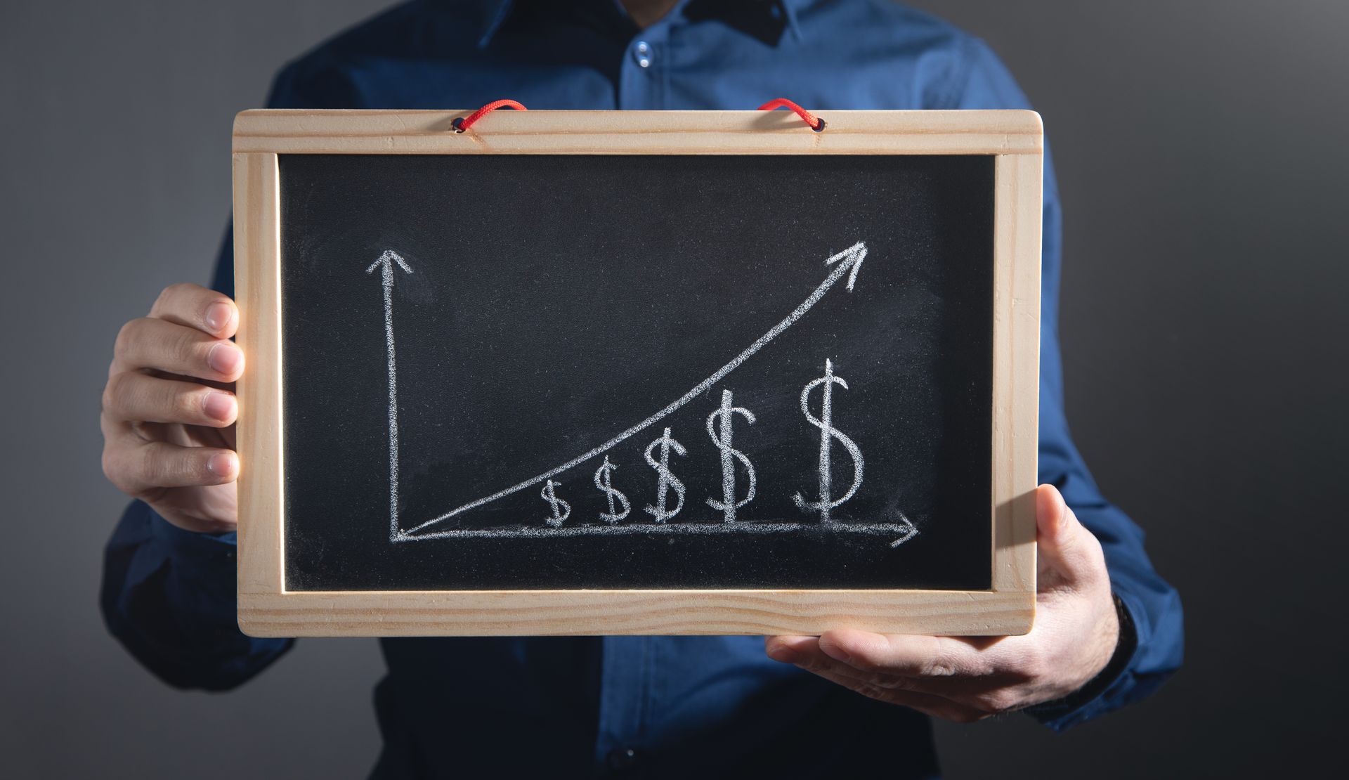 Person holding a chalkboard with an upward trend graph and dollar signs.