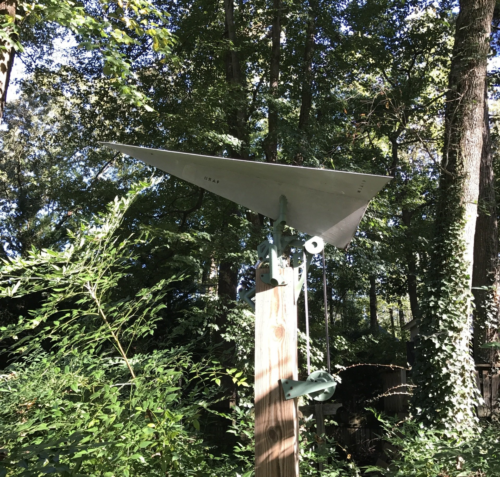 A paper airplane is sitting on a wooden post in the woods