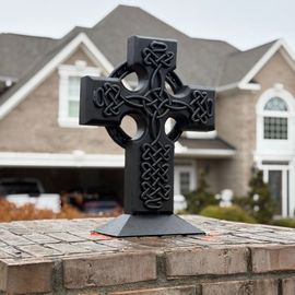A black cross is sitting on a brick wall in front of a house