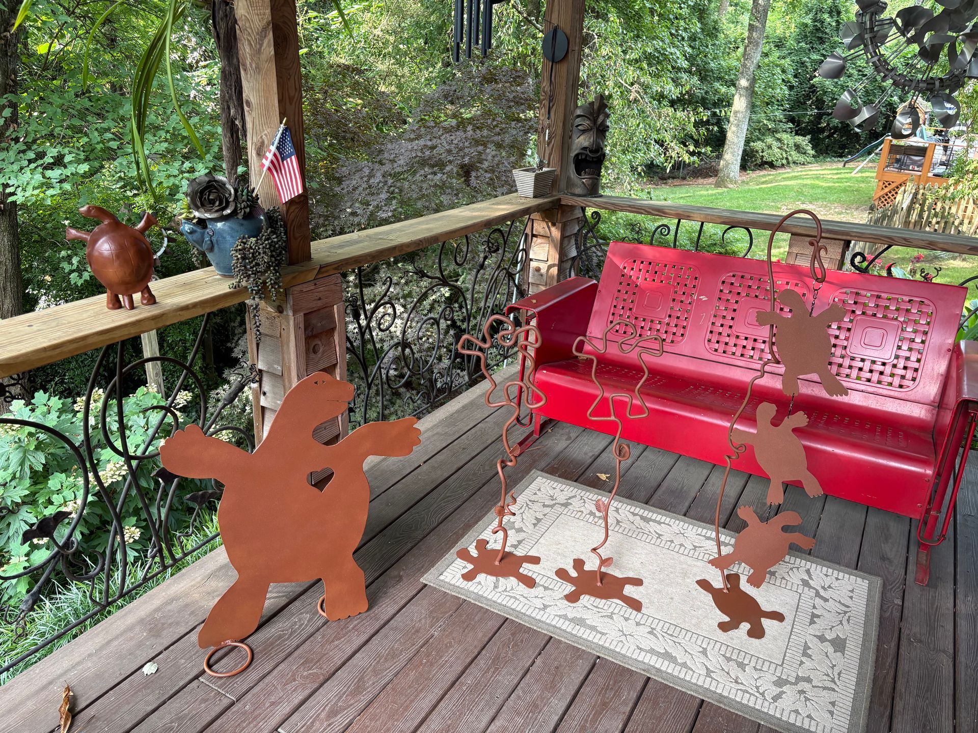 Outdoor porch with red metal bench, wooden bunny cutouts, and a patterned rug amid trees.