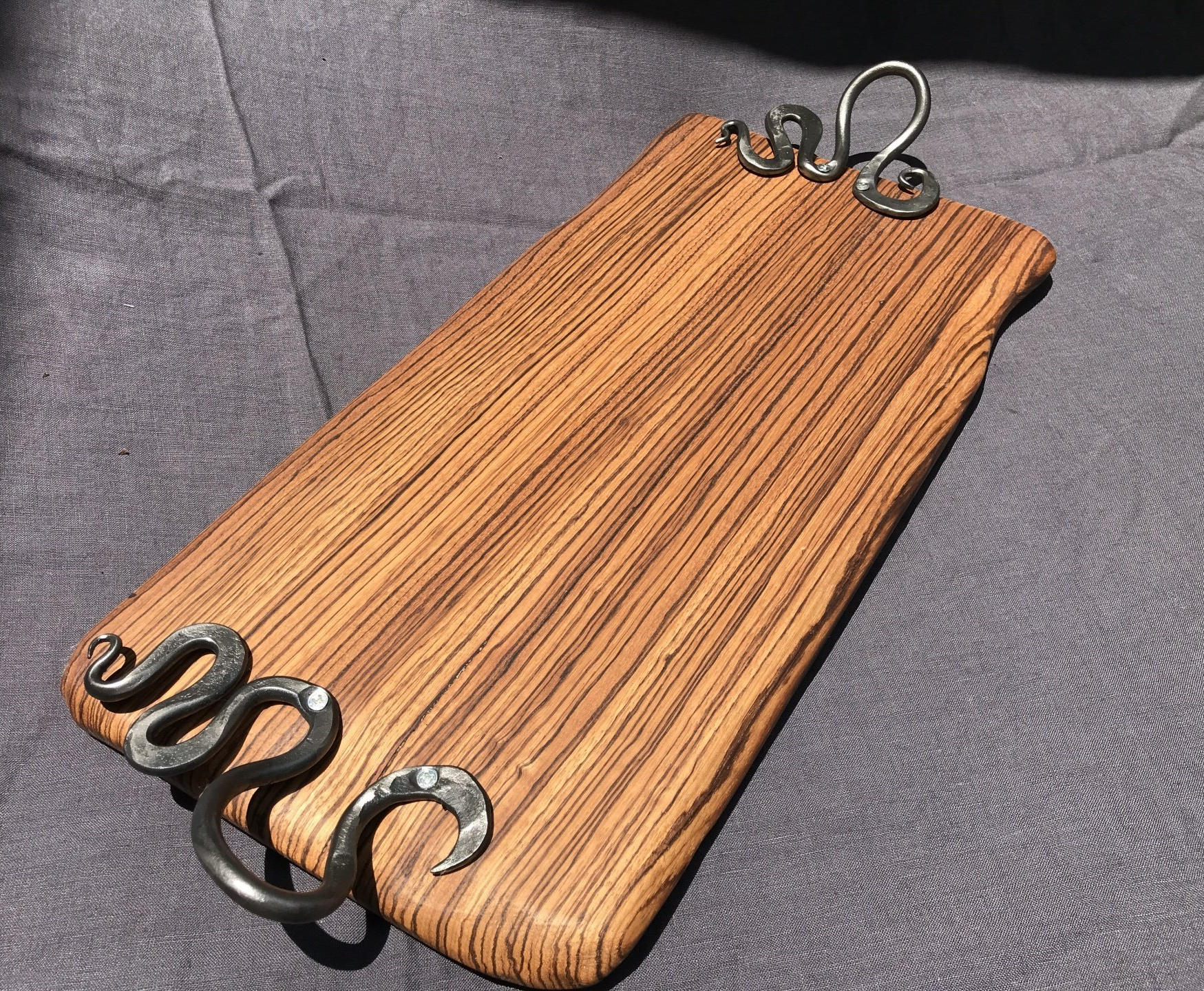 A wooden cutting board with metal handles is sitting on a table.