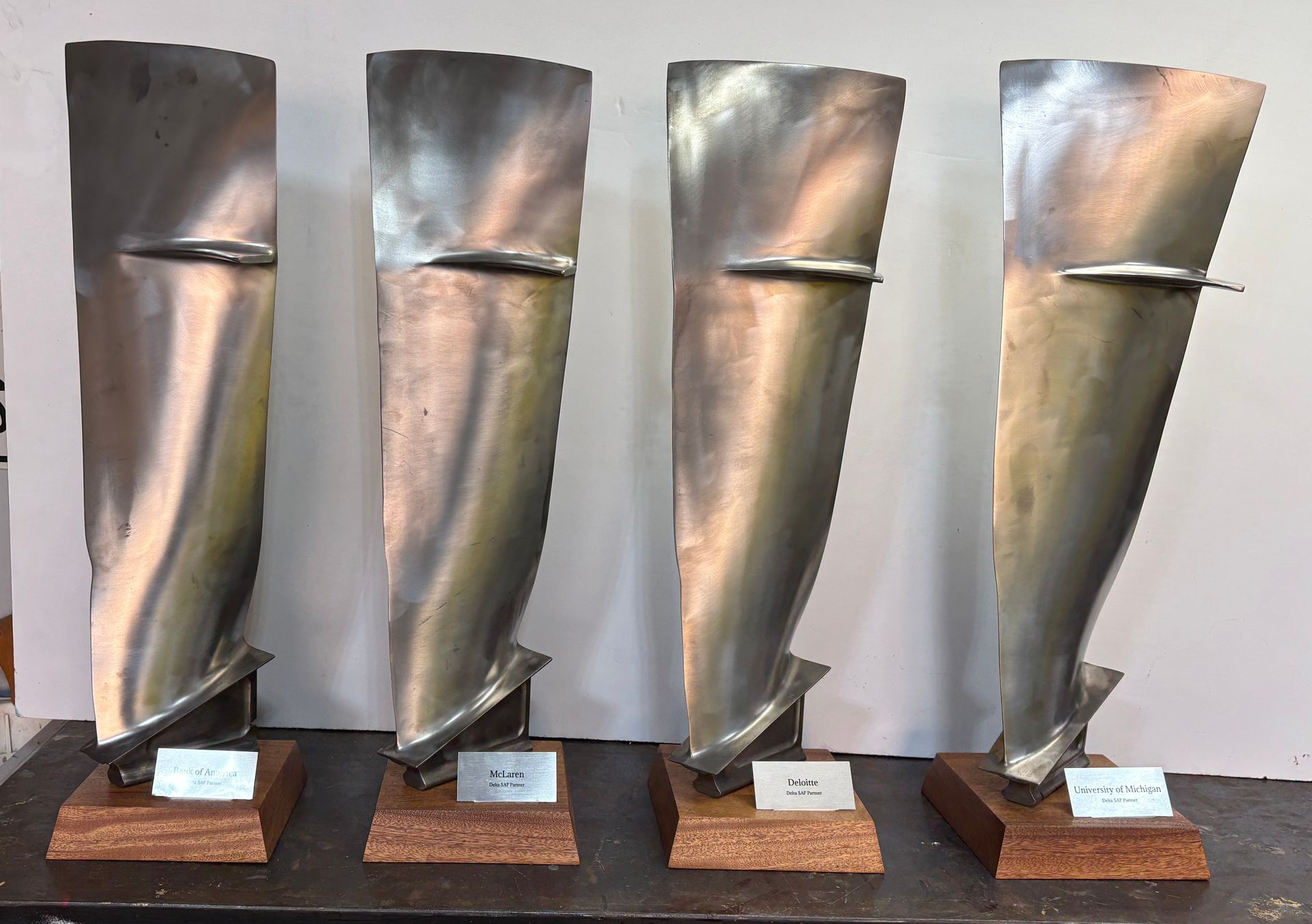 Four metallic turbine-like sculptures on wooden bases lined up against a light background.
