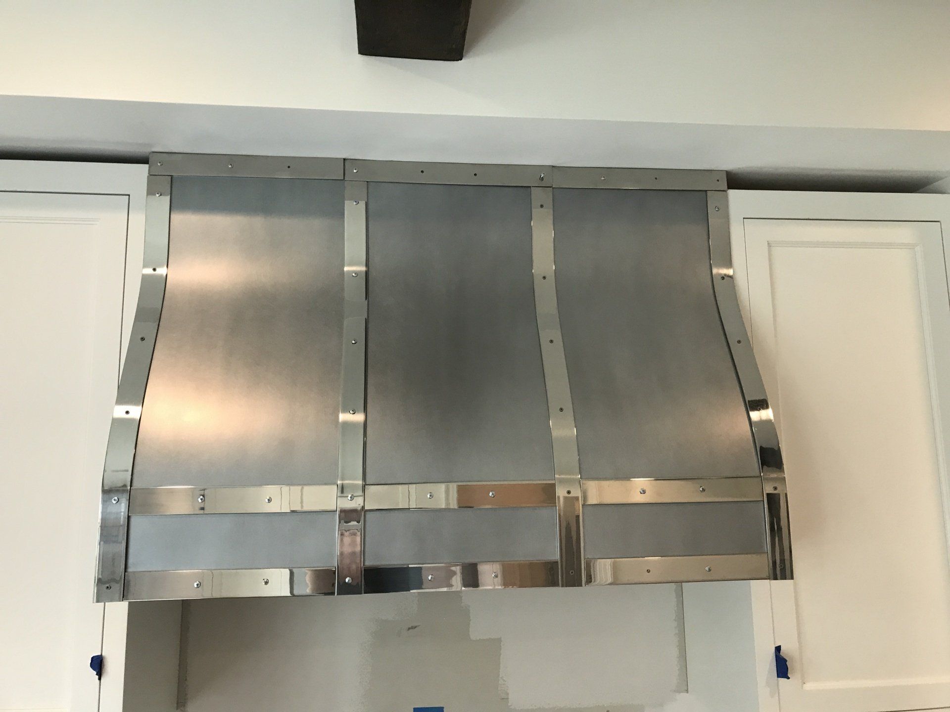 A stainless steel hood in a kitchen with white cabinets