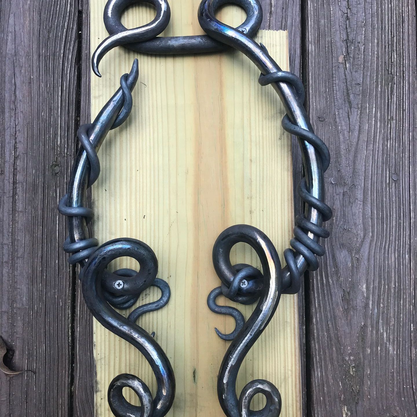 A pair of wrought iron door handles on a wooden board.