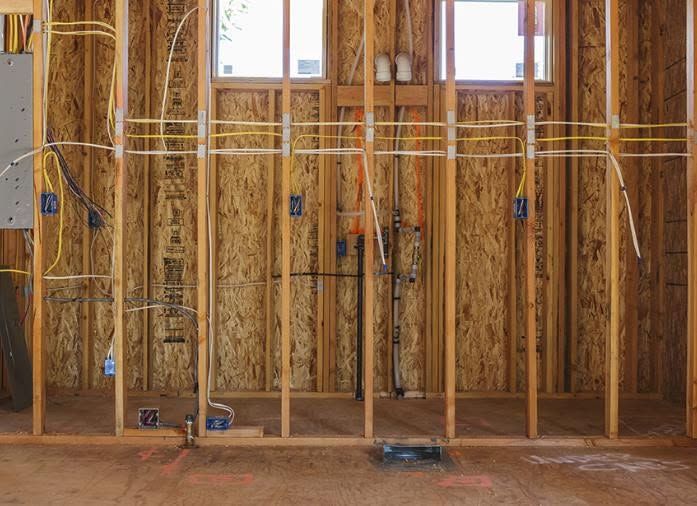 Framed wall under construction with exposed studs, wiring, insulation, and two windows above.