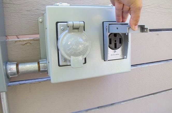 Outdoor electrical outlet and covered light fixture on a beige wall, with a hand opening the outlet cover.
