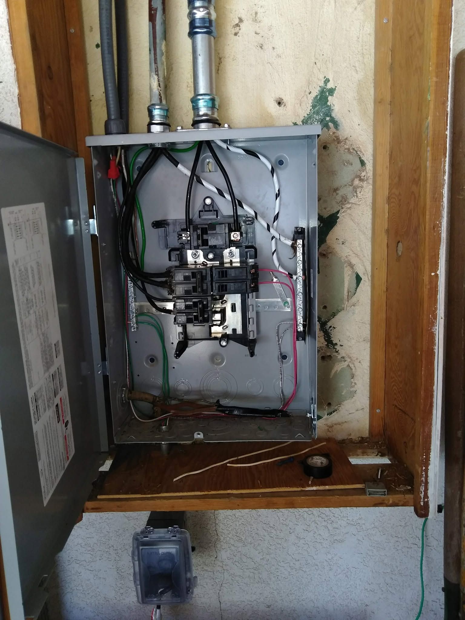 Open electrical panel with exposed wiring and breakers in a wall alcove