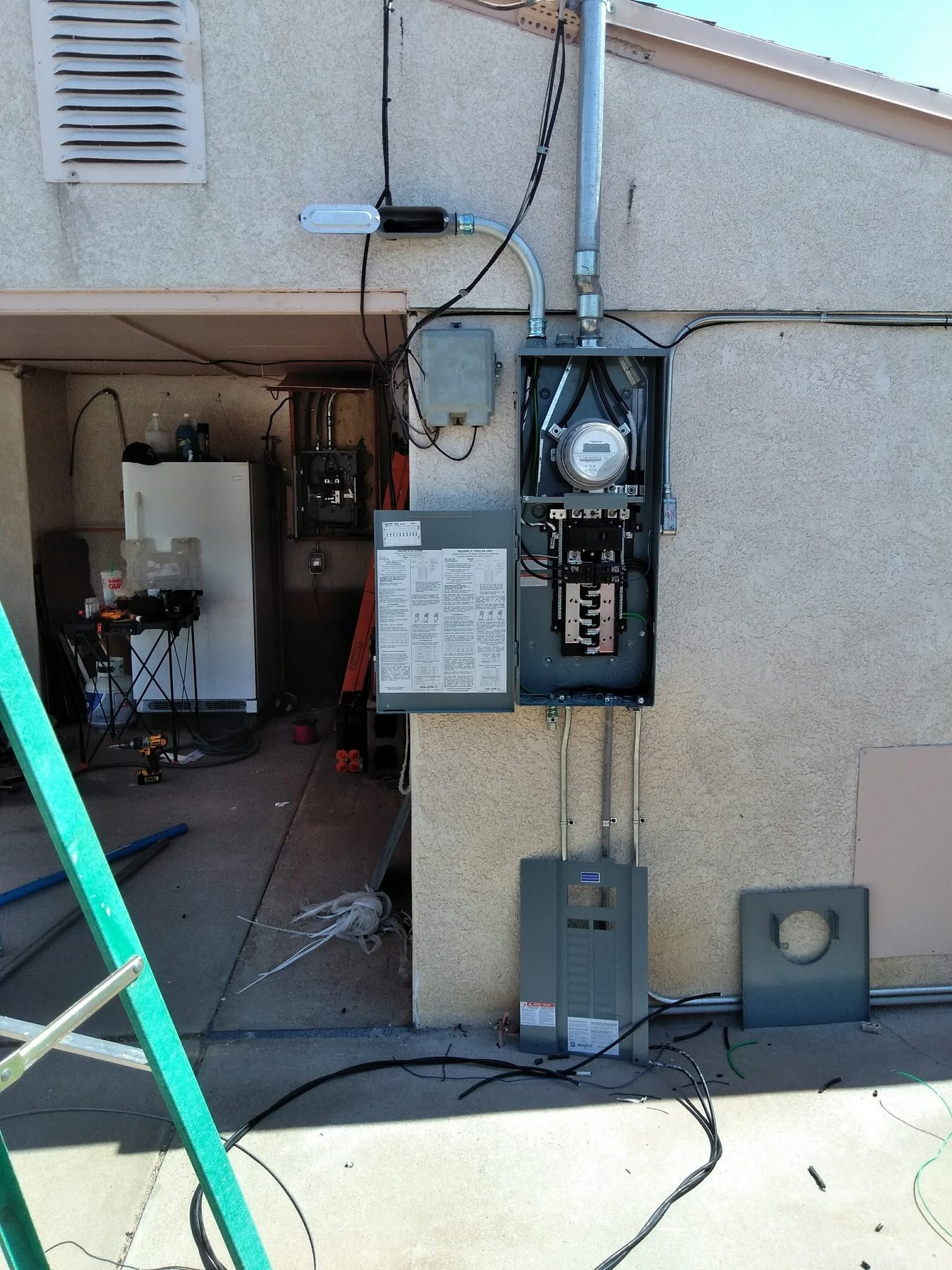 Open electrical meter and service boxes mounted on an exterior stucco wall near a garage.