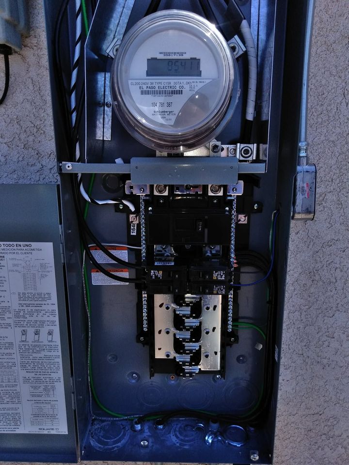 Open electrical meter panel with wiring and circuit breakers inside a gray utility box