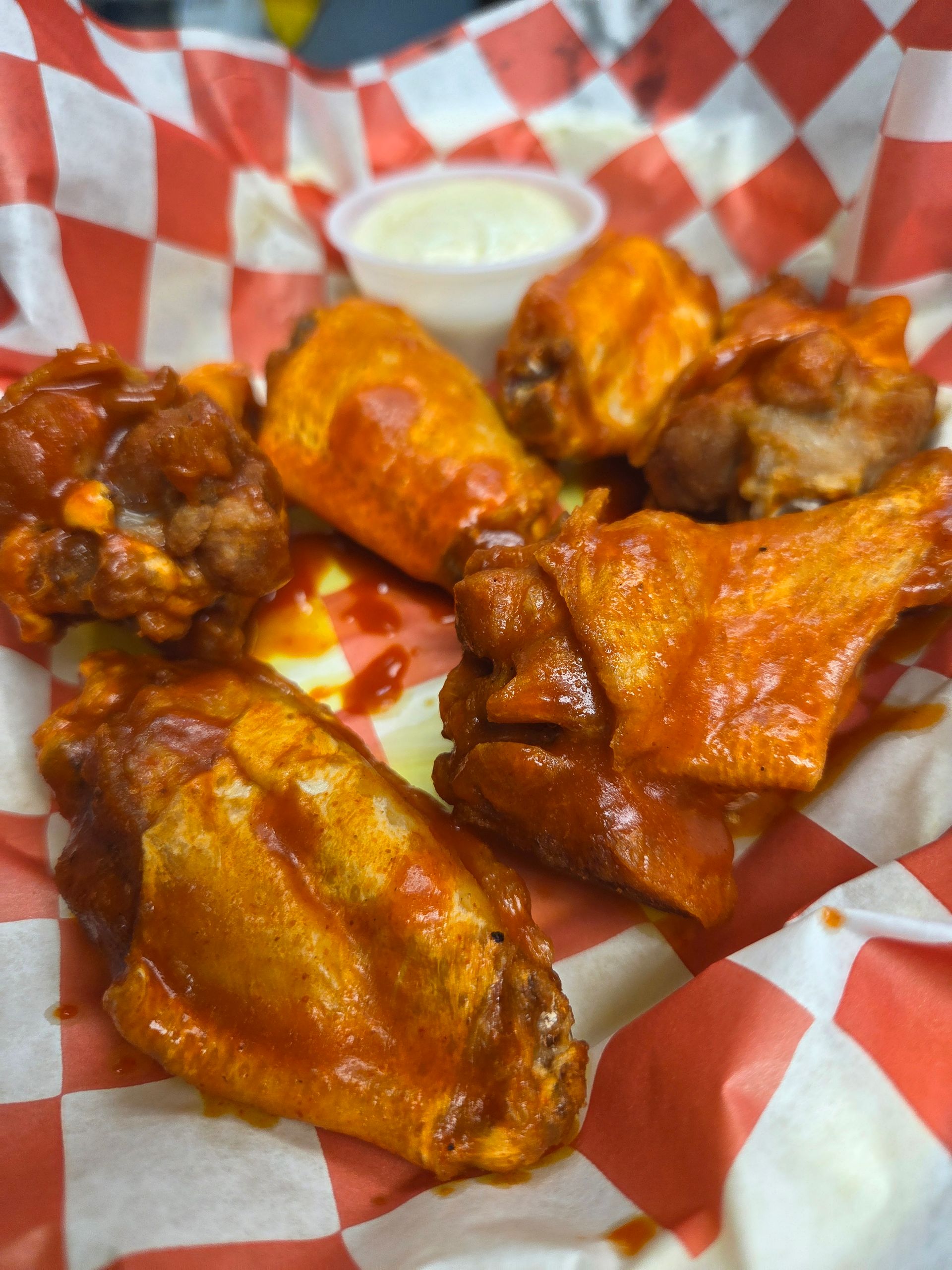 Red sauce covering chicken wings with a with a side of white sauce on the side