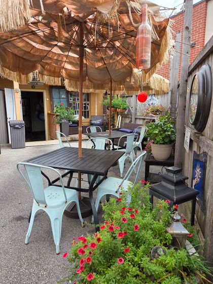 Outdoor seating area with tables, chairs, thatched umbrellas, and decorative plants.