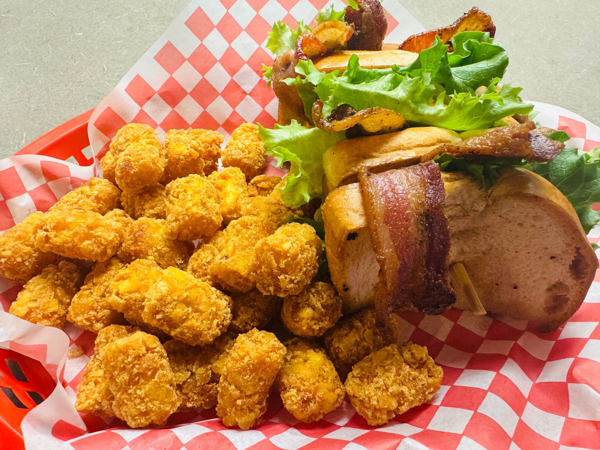 BLT sandwich with bacon over the side of the bread and lettuce peeking out with a side of tater tots