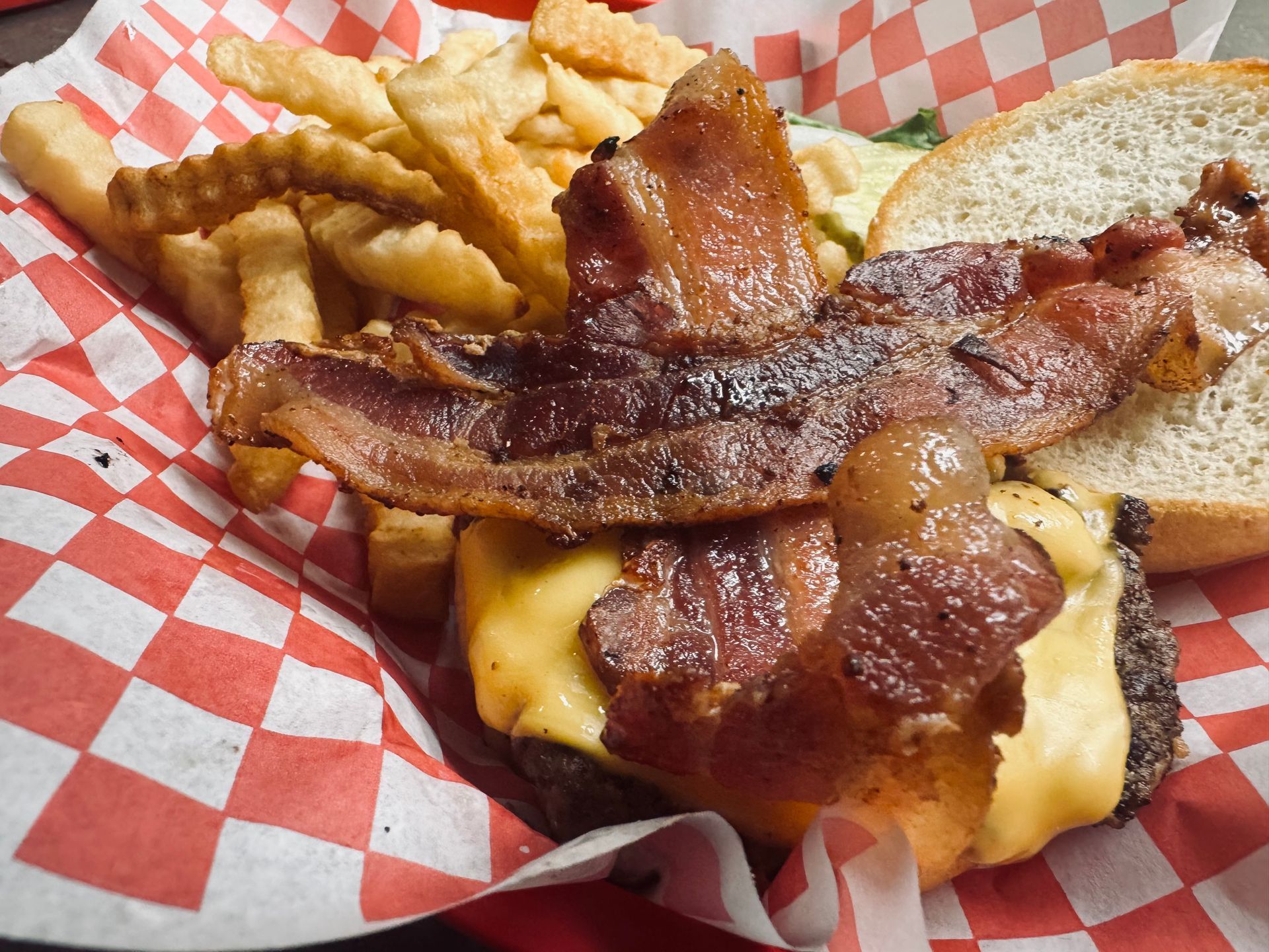 Crispy bacon in the foreground with cheese and a burger patty underneath with a side of crinkle fries