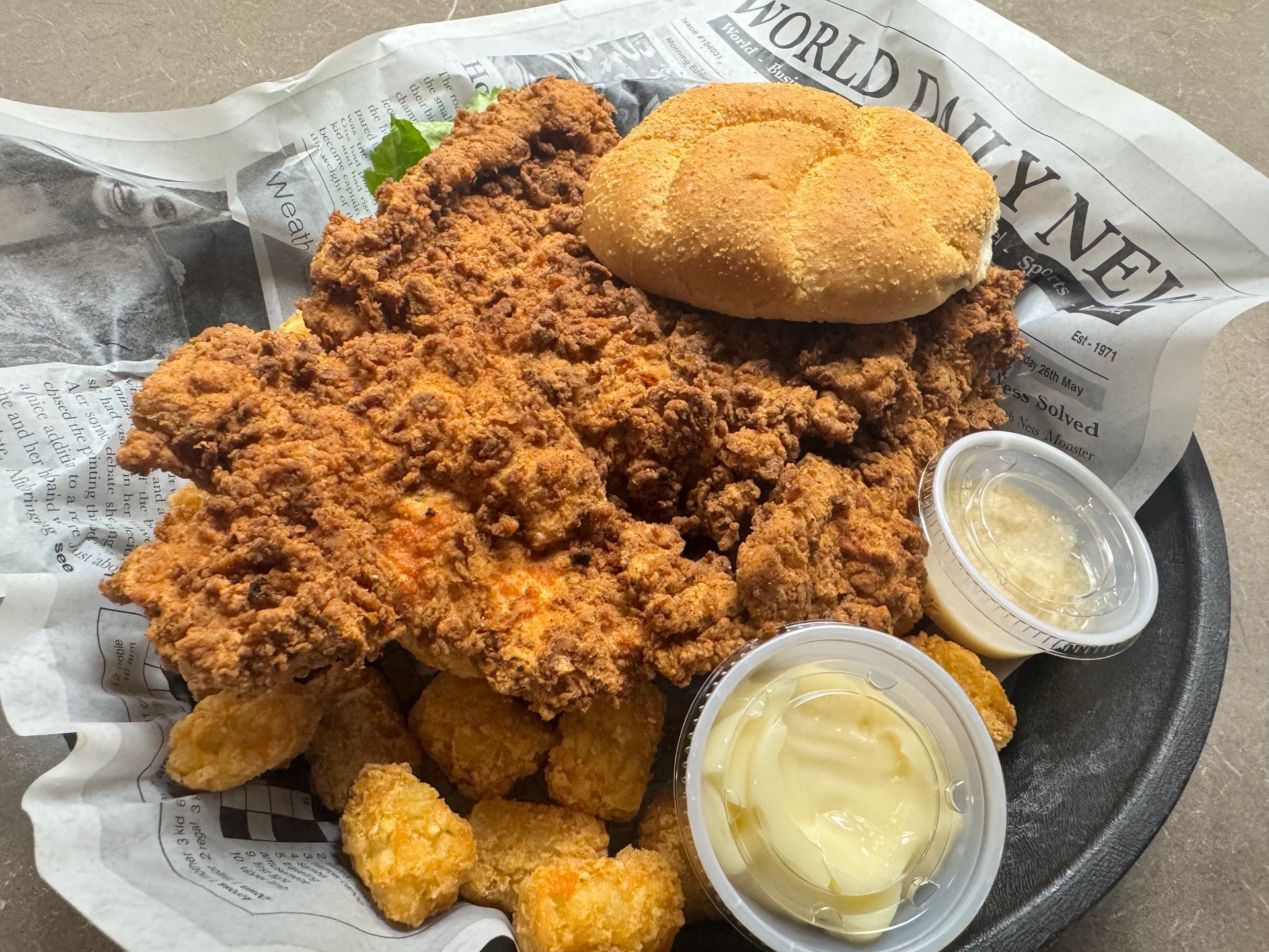 Generous portion of a tenderloin with a side of bread and tater tots with a horsey sauce and horseradish.