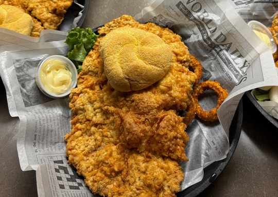 Plated fried chicken with dipping sauce, on newspaper-lined trays.