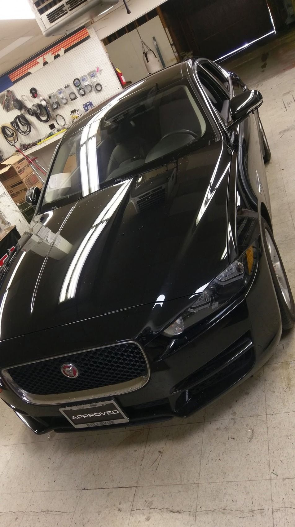 Black Jaguar sedan in a showroom, angled front view with glossy finish and bright overhead reflections