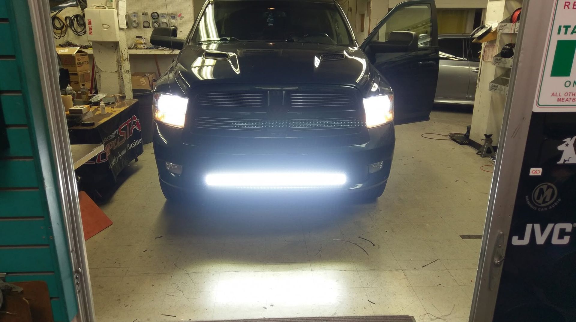 Black SUV in a garage with headlights and bright fog light on, viewed from the front.