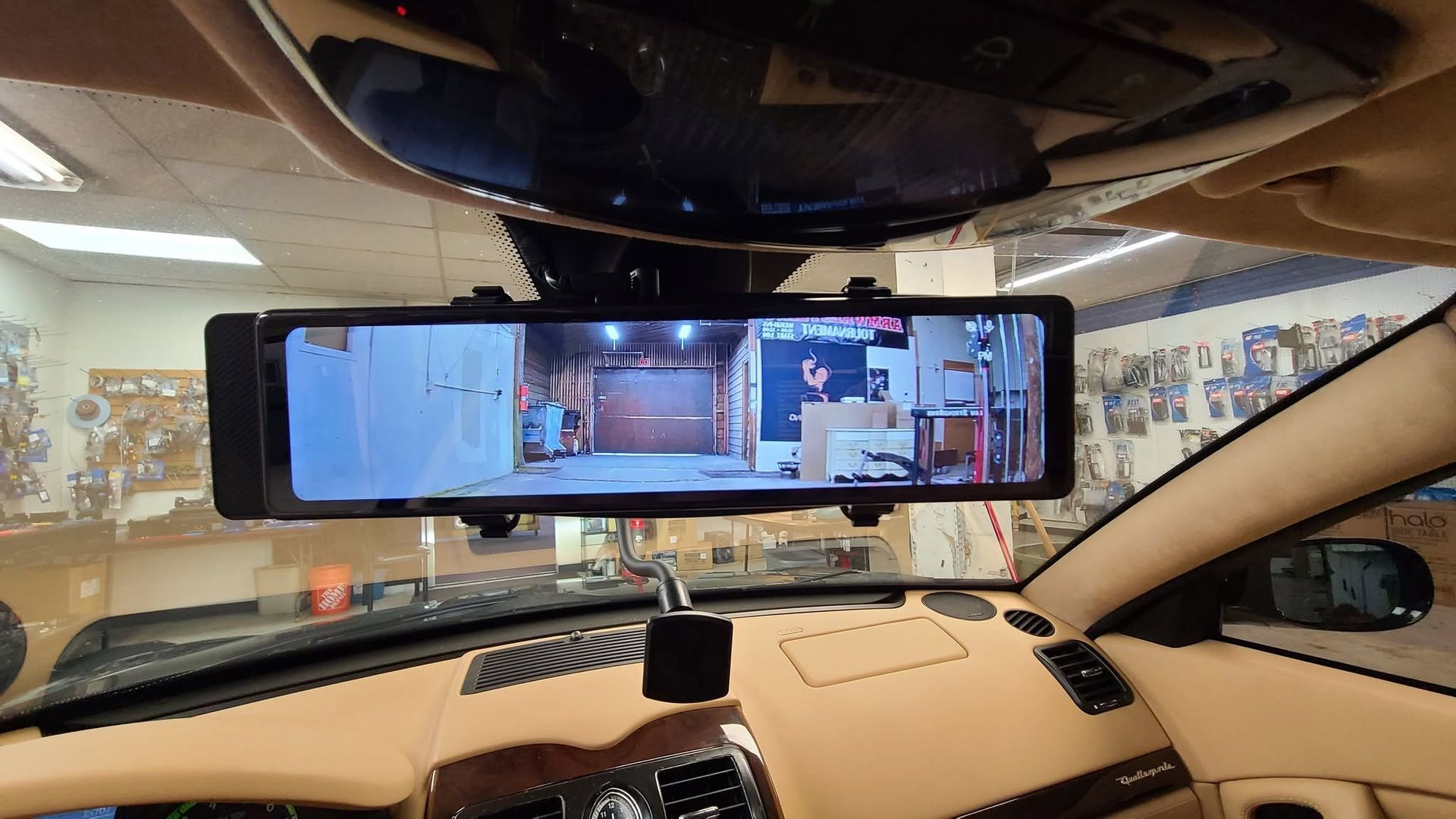 Inside a car, a phone mounted on the dashboard displays a live view of a garage or parking area.