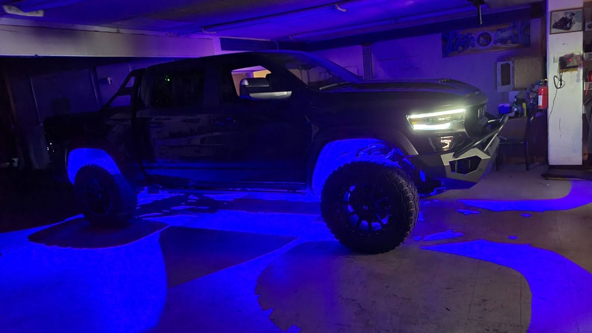 Black pickup truck in a garage, lit by blue underglow and bright headlights.