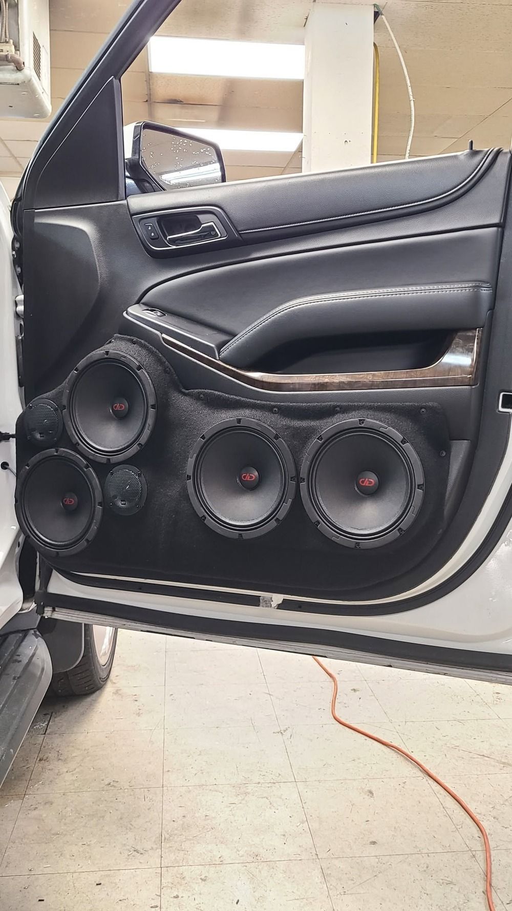 Open car door with custom black speaker panel and multiple large audio speakers installed.