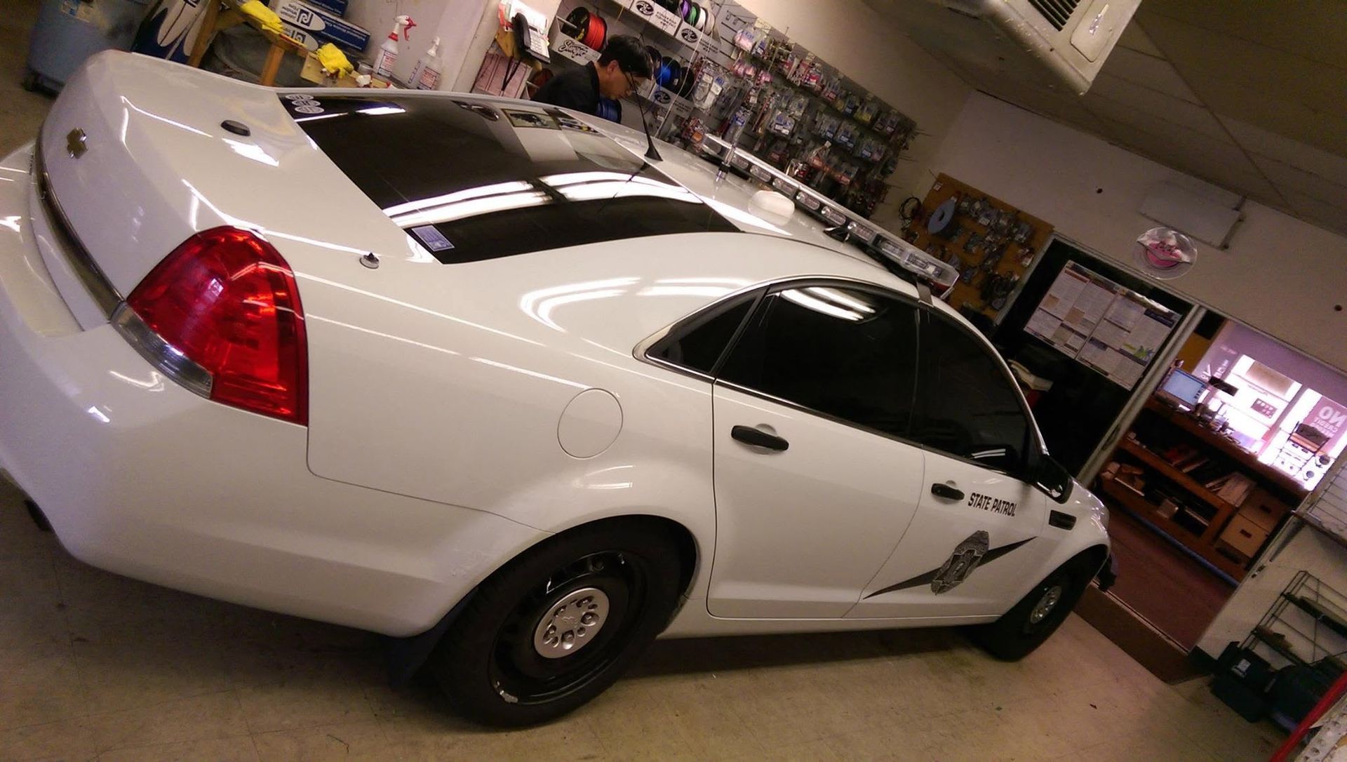 White sports car displayed indoors in a showroom, with a black hood stripe and red taillights.