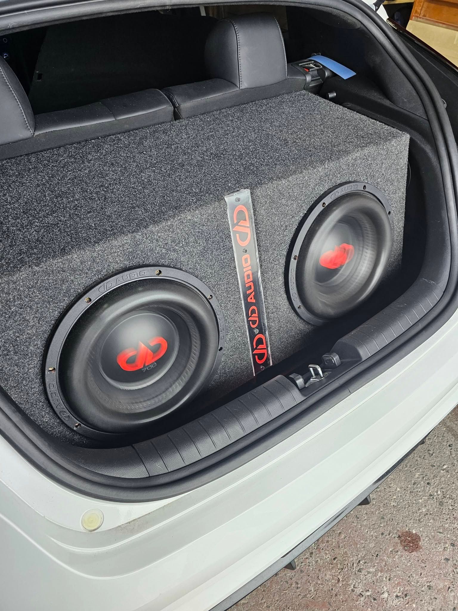 Two subwoofers in a gray carpeted car trunk enclosure