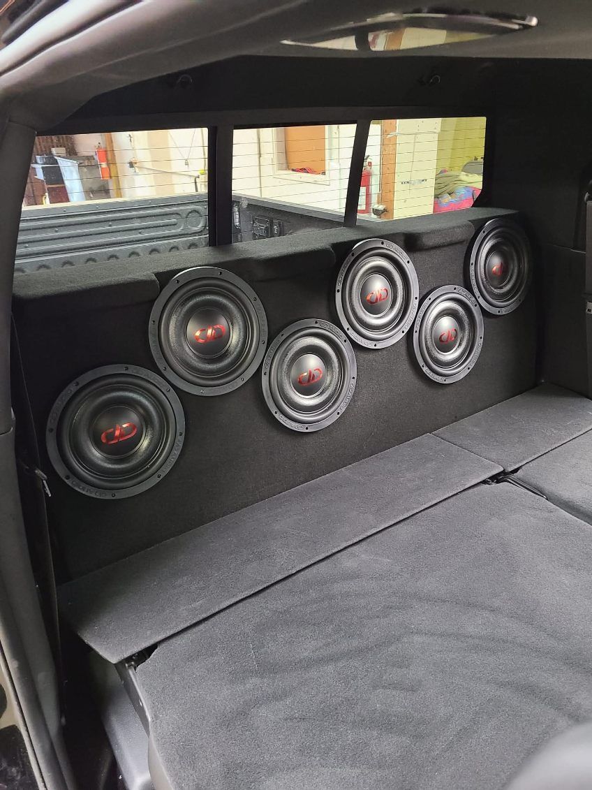 Car audio setup with six speakers mounted in a black rear panel and folded seat in foreground