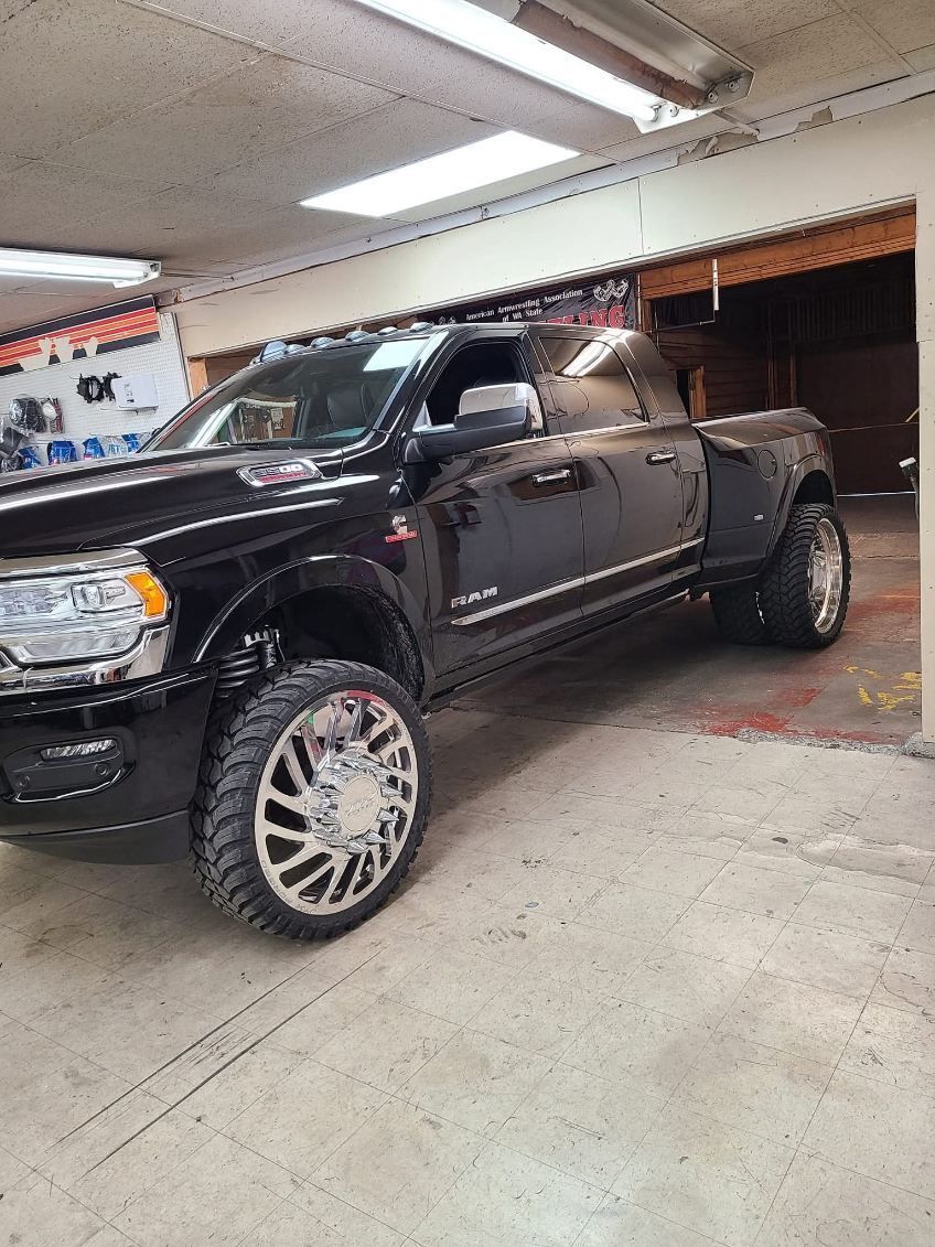 Black pickup truck parked inside a garage, viewed from the side under fluorescent lights.