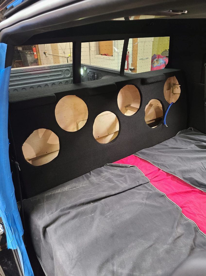Interior of a car with a black panel of circular cutouts behind the seats and gray-pink upholstery